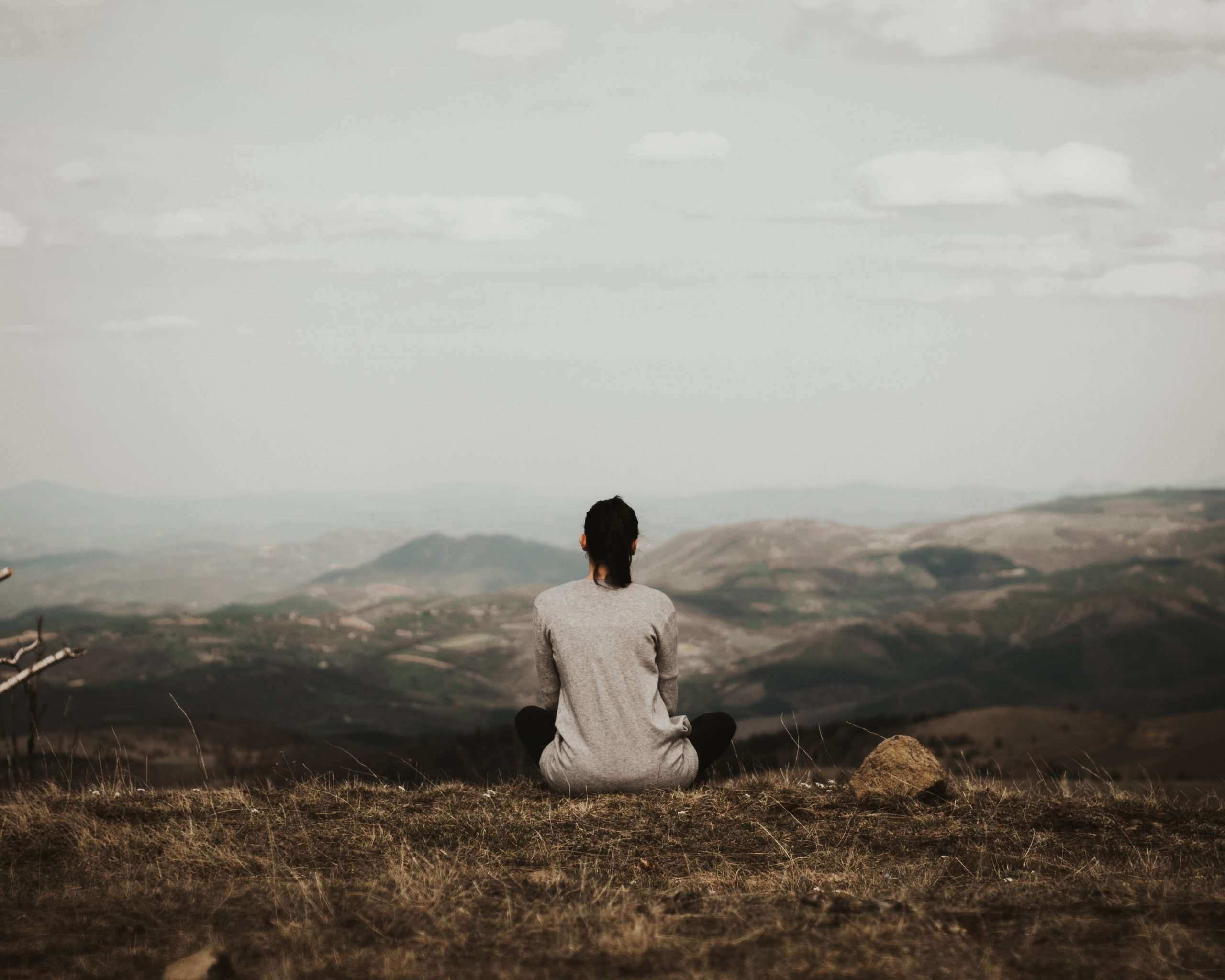 woman-sitting-on-hilltop-from-behind