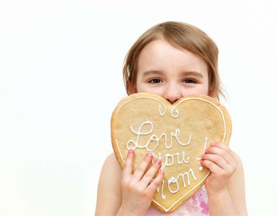 little-girl-giant-cookie-covering-half-her-face-heart-shaped-love-you-mom-icing-letters-mothers-day-blog-post