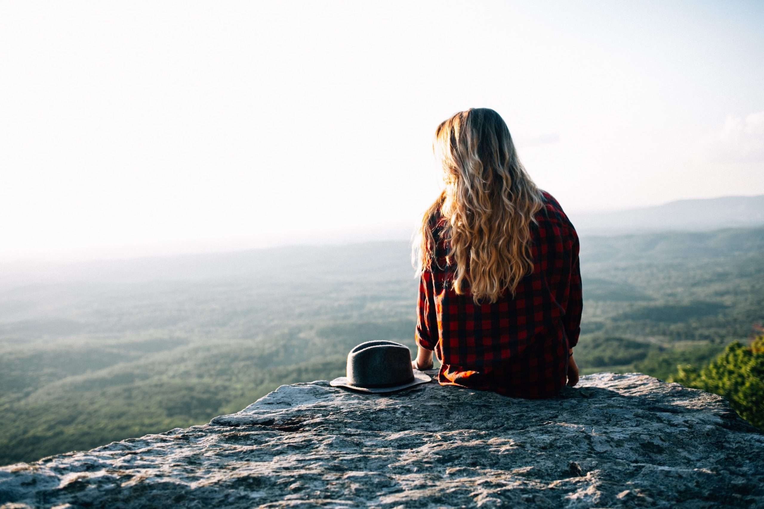 woman-sitting-on-rock-from-behind-long-blonde-hair-red-jumper-in-mindful-mood