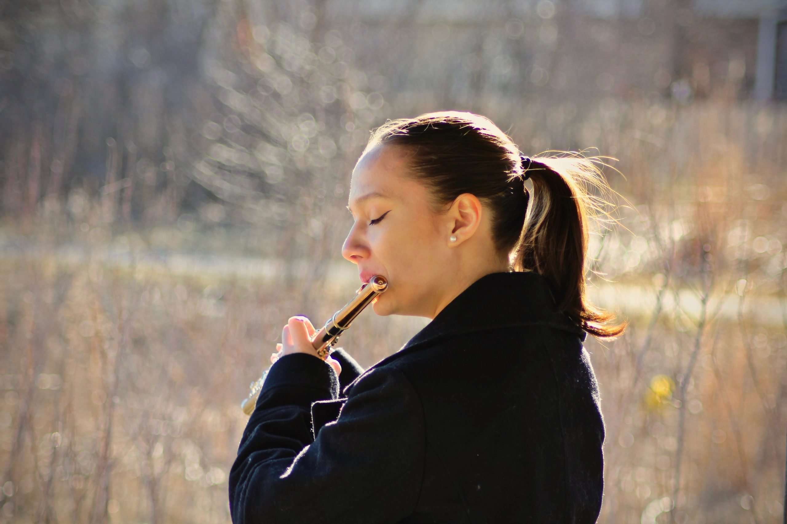 woman-dark-ponytail-playing-flute-in-open-field-eyes-closed-in-flow-state