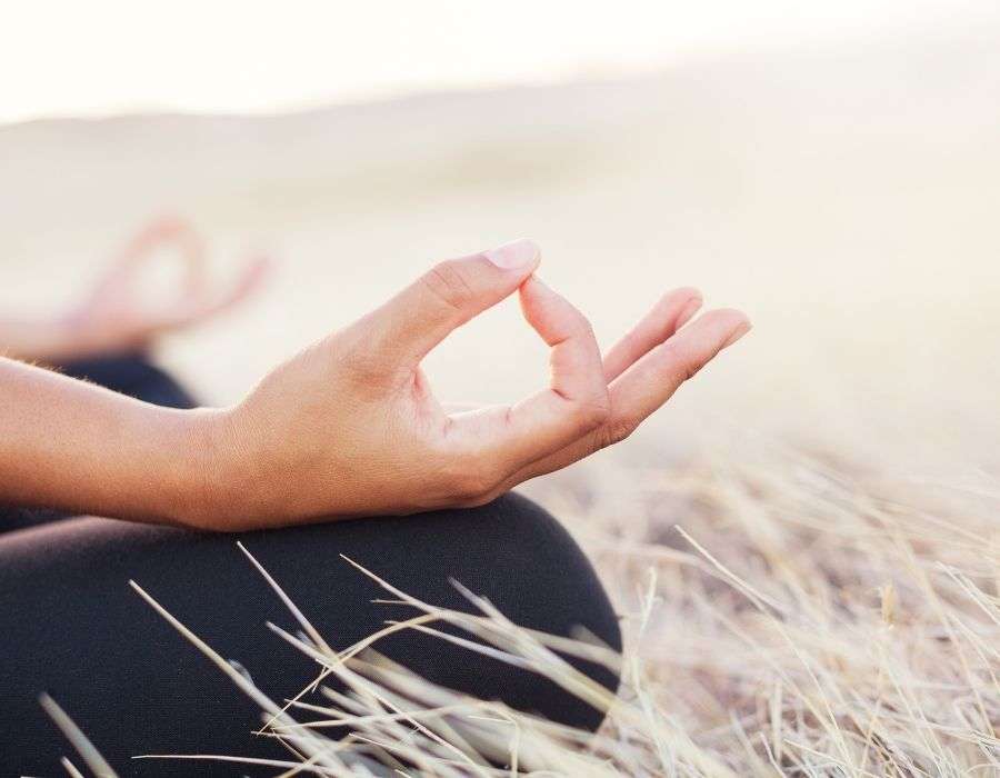 close-up-hand-on-crossed-knee-meditation-pose-sitting-in-field-benefits-of-meditation-blog-post