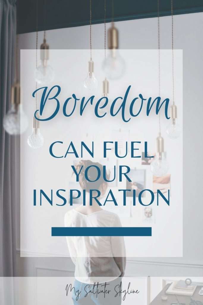 woman-from-behind-brown-hair-in-bun-staring-at-collage-of-pictures-on-wall-for-inspiration-multiple-dangling-lights-hanging-from-ceiling-boredom-for-inspiration-blog