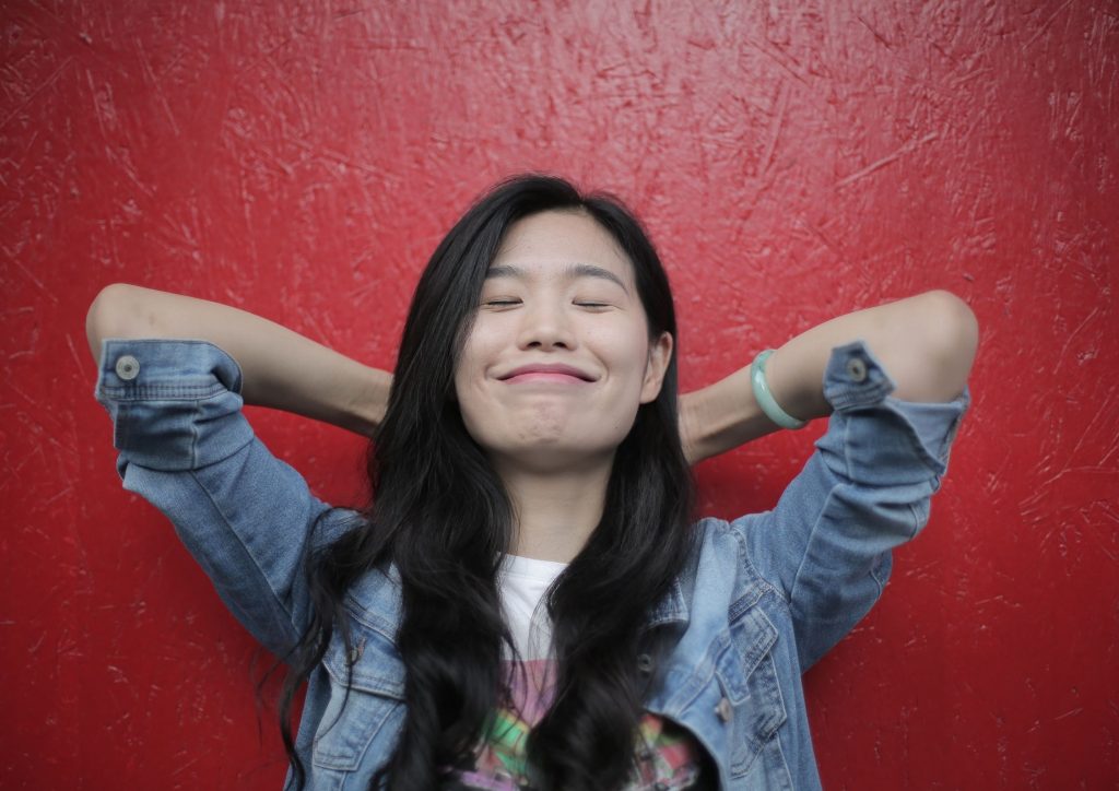 woman-long-dark-hair-hands-behind-head-smiling-content-with-life