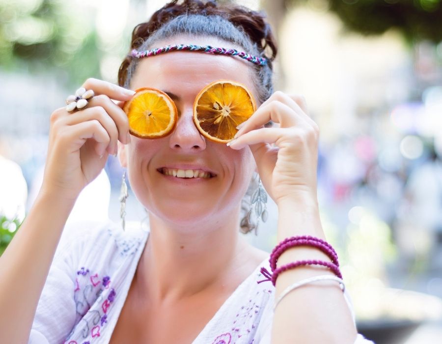close-up-woman-hair-tied-back-holding-orange-slices-up-to-eyes-smiling-be-athentic-blog-post