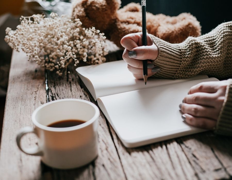 close-up-arms-in-jersey-writing-on-notebook-coffee-close-by-letter-to-future-self-blog